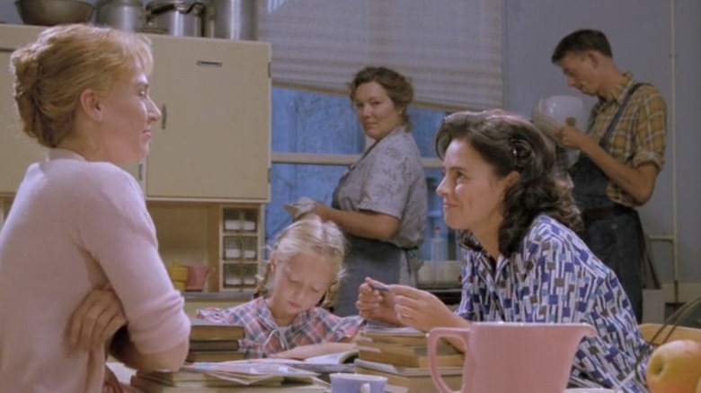 Elsie de Brauw asa Lara and Els Dottermans as Danielle smiling at each other across a table while Carolien Spoor as Thérèse reads a book and Willeke van Ammelrooy as Antonia looks on from the kitchen sink in Antonia's Line