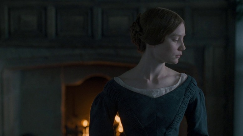 Mia Wasikowska as Jane Eyre standing by a fireplace in the dark in Jane Eyre