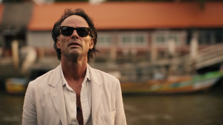 Walton Goggins' Rick, in sunglasses and a white suit, looks slightly upwards in The White Lotus