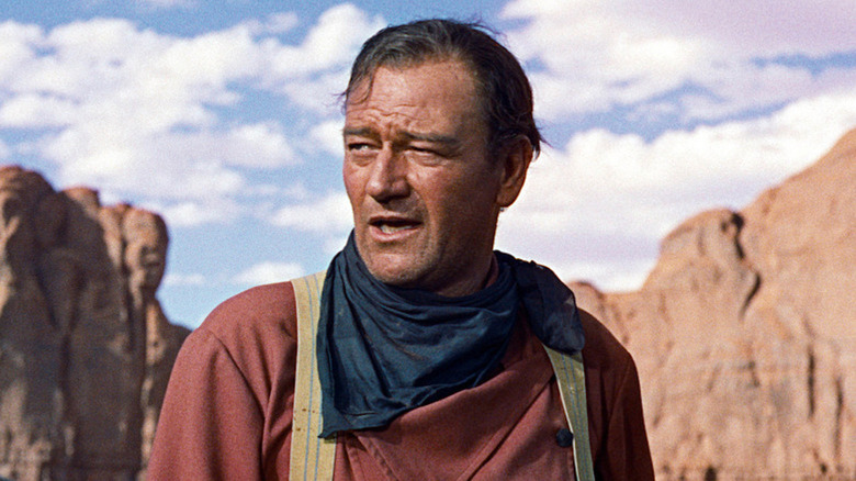 Ethan Edwards standing in front of some sand-colored rocks in The Searchers